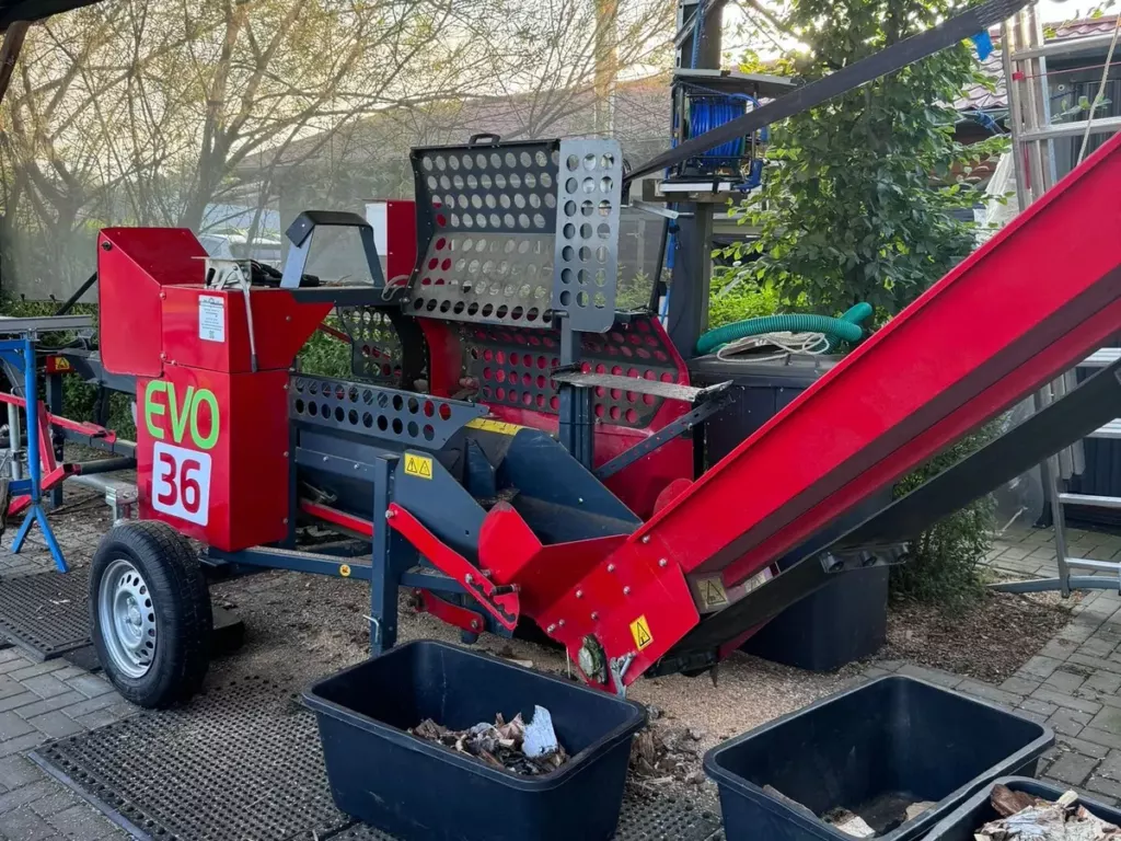 Roter Sägespaltautomat mit Förderband unter dem Vordach
