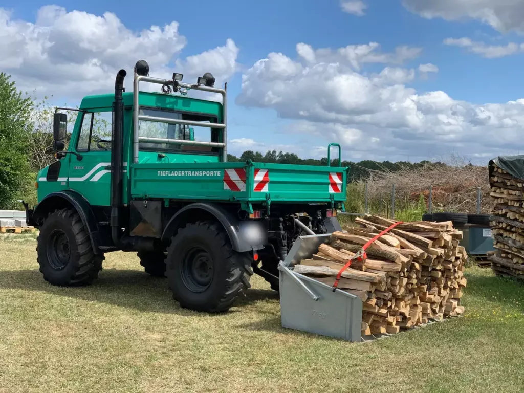 Unser grüner Mercedes-Benz Unimog U1400 neben einem Bündel gespaltener Scheite
